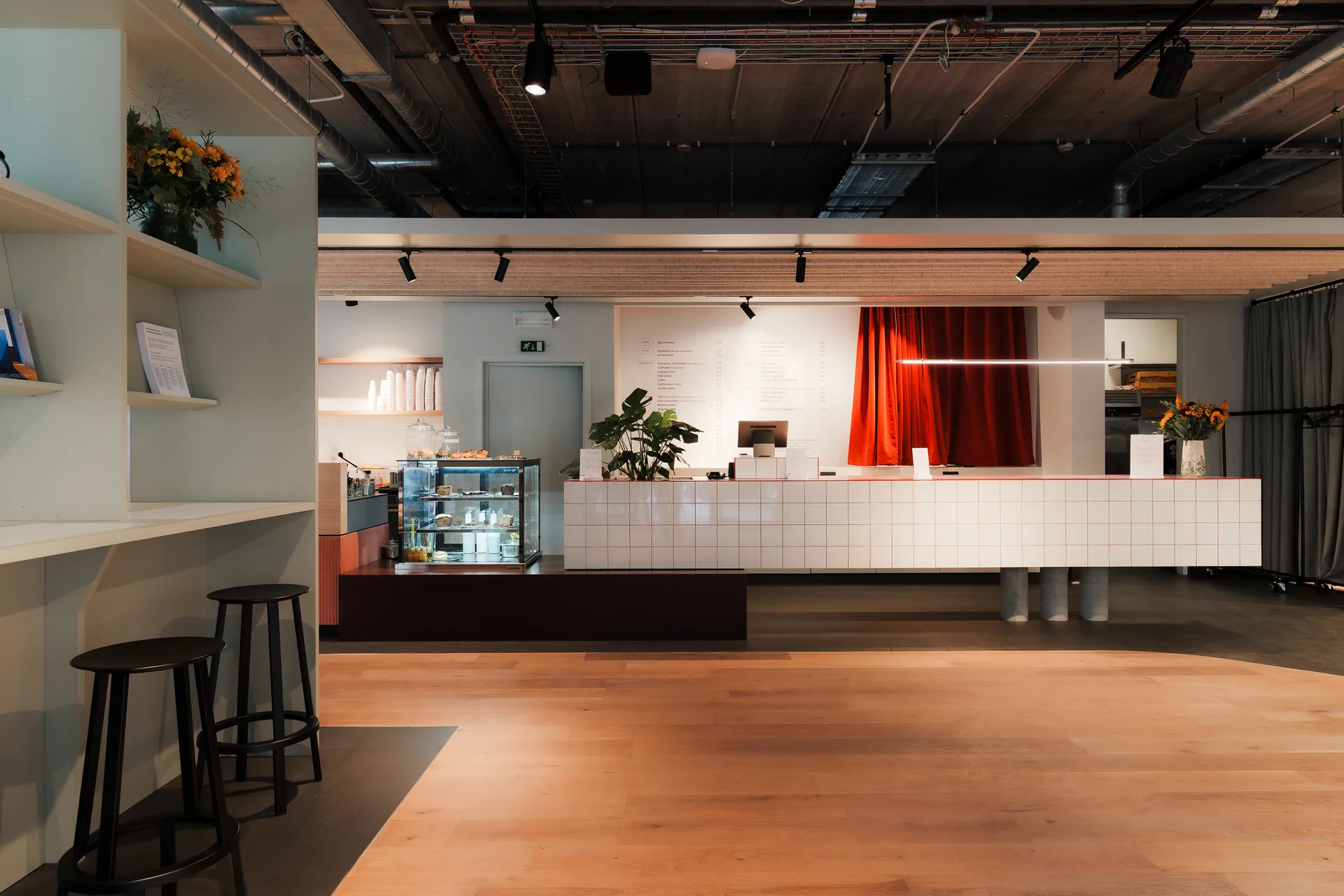 The counter at Bump&rsquo;s Caf&eacute; Concept &mdash; a long white tiled bar with open shelving, a pastry case and a red curtain behind