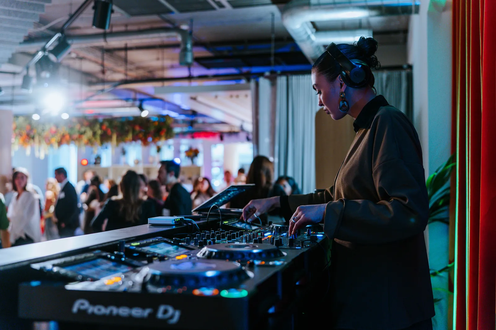 A DJ at the decks during an evening event, the crowd behind under coloured light