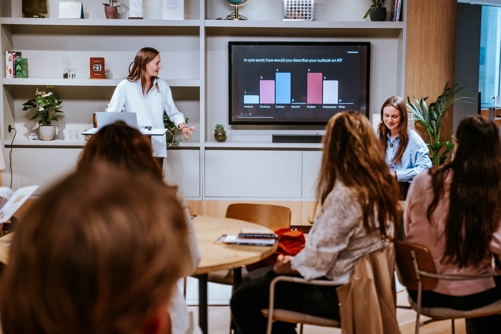 A speaker presenting to a seated group, a chart on the screen behind her