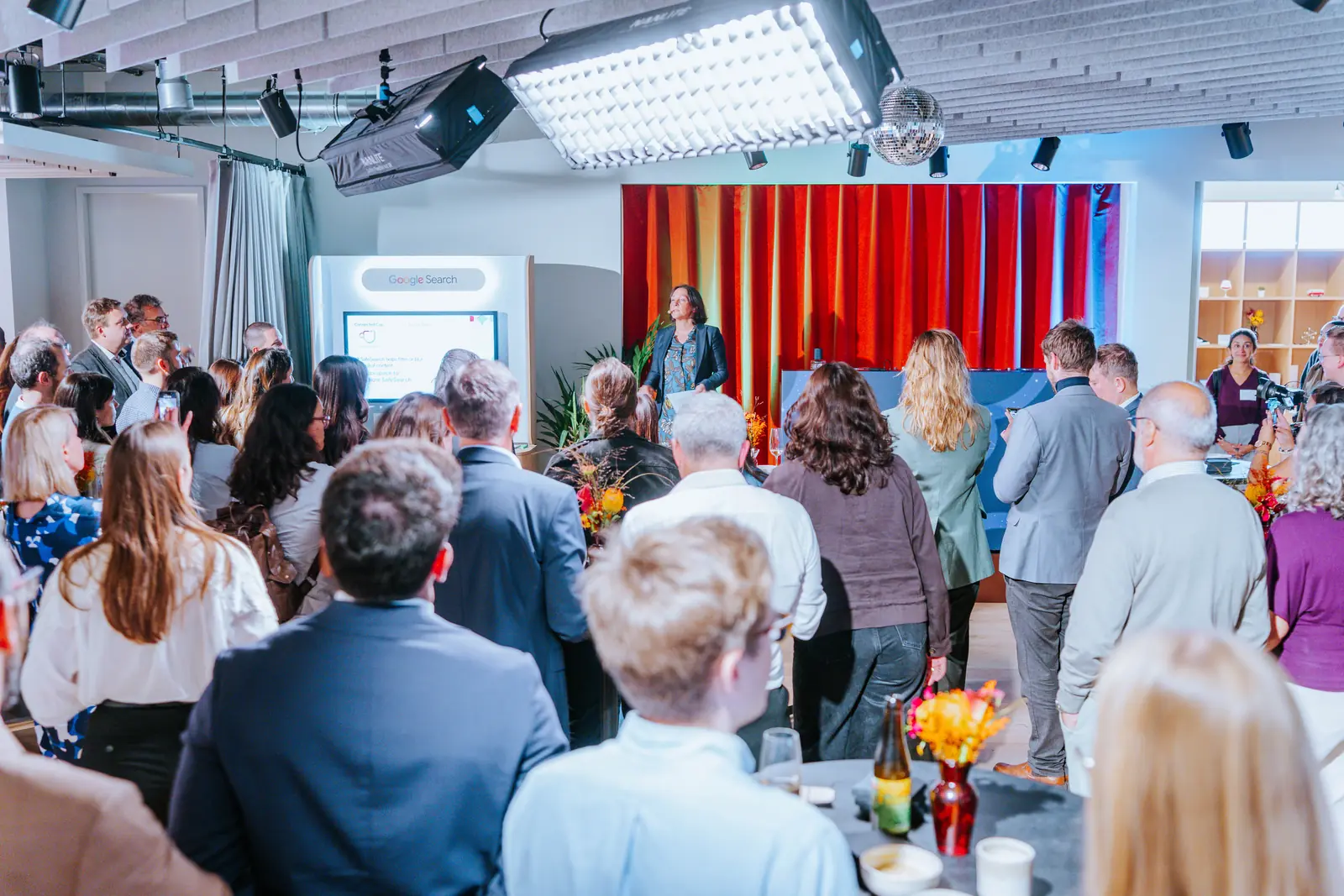 An evening audience gathered in front of the stage, drinks in hand